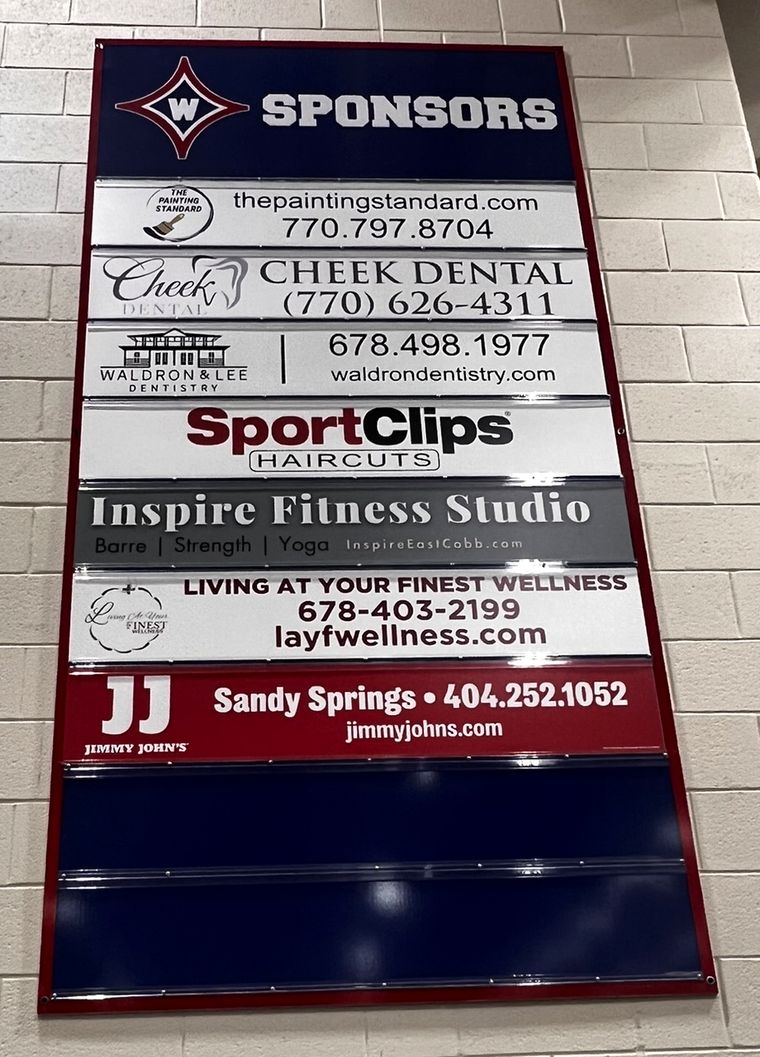 Sponsor board in the Walton HS main gym showing local business plates, with open slots at the bottom