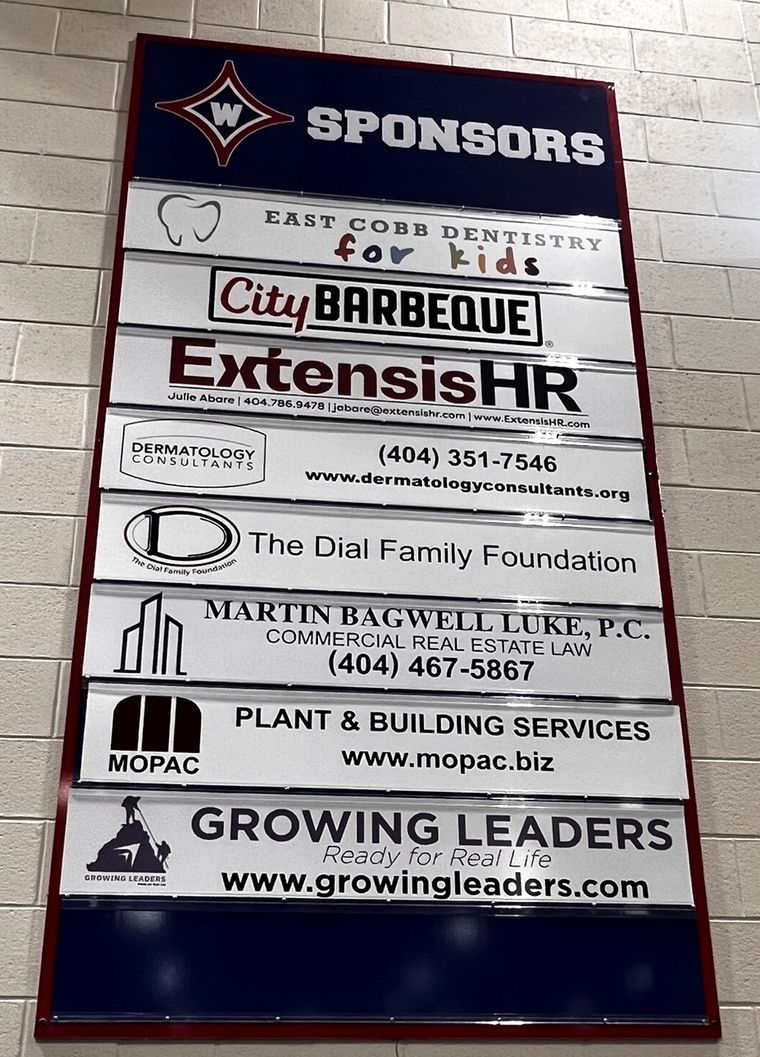Second sponsor board in the Walton HS main gym showing local business plates, with an open slot at the bottom